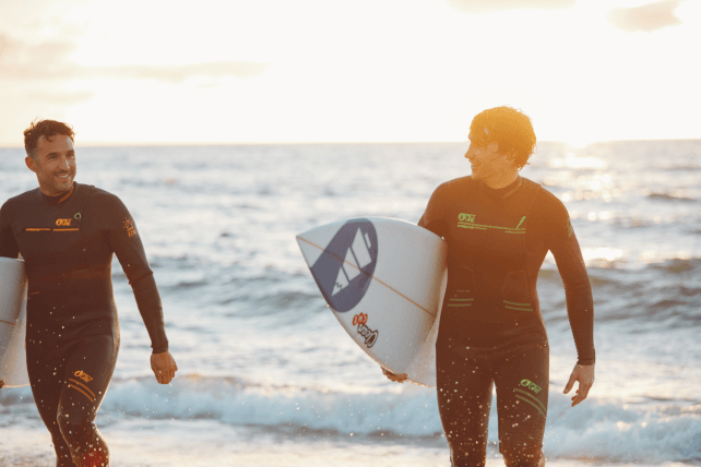Surfers on the beach at sunset with Picture Organic Wetsuits
