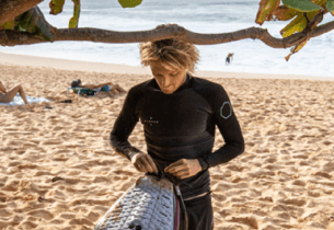 Surfer with neoprene top from Vissla on the beach with surfboar