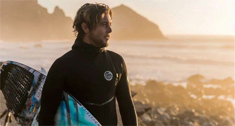 Surfer mit Rip Curl Wetsuit und Surfboard unterm arm beim Sonnenuntergang